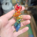 A single 3-inch rainbow glass spinner infused with cremation ash, featuring swirling red, orange, yellow, green, and blue colors, shown resting in a person's hand.