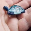 Handcrafted glass sea turtle cremation pendant shown from a low side angle, featuring deep blue flippers and a domed aqua shell filled with white flecks of encased cremation ashes, resting in the hand to show size and detail