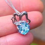 Close-up of a silver butterfly cremation pendant held between fingers, featuring a sparkling blue dichroic memorial stone infused with cremation ash, set beneath delicate sculpted butterfly wings on a fine silver chain