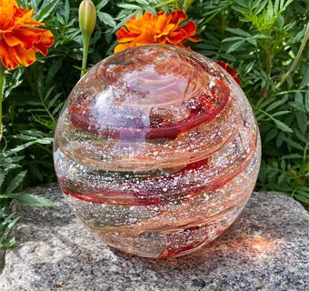 Gold sparkle infinite staircase cremation paperweight with visible cremation ash displayed outdoors among orange flowers