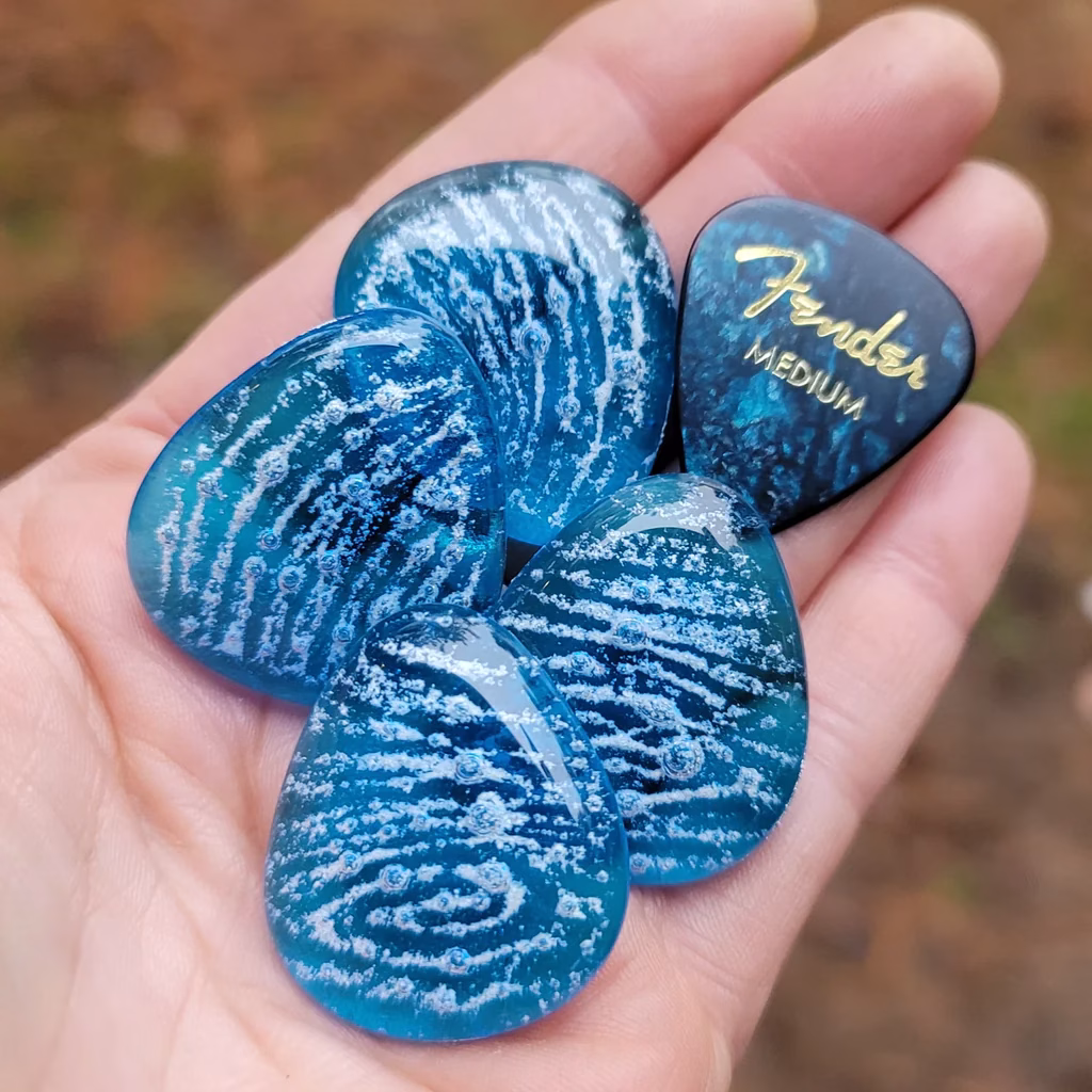 Glass Guitar Pick Cremation Stone Set in deep blue tones with ashes suspended in swirling patterns, shown in the palm of a hand, by Sands of Time.