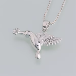 Polished silver hummingbird cremation pendant shown in mid-flight, with detailed wings and a small flower held at its beak, hanging from a silver chain.