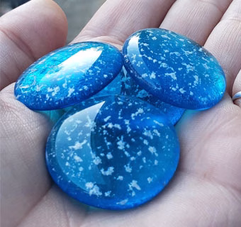 Set of 4 blue glass cremation stones with visible cremation ash resting in the palm of a hand