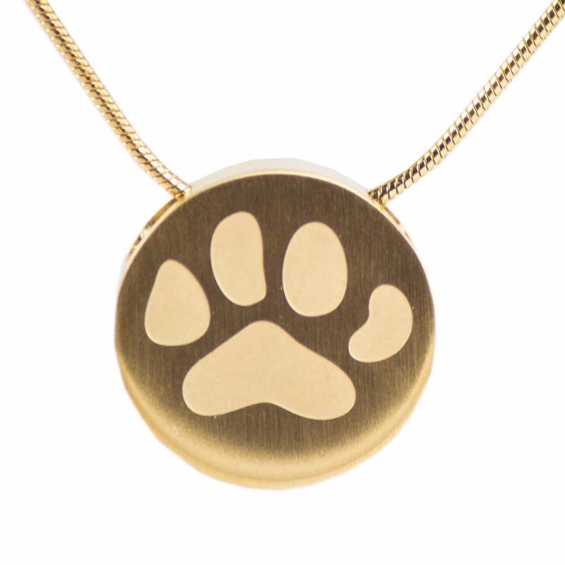 Close-up view of a round bronze cremation necklace featuring a large engraved paw print, shown on a silver snake chain against a white background.