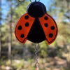 Ladybug suncatcher with vibrant orange wings and black spots, handcrafted with cremation ash and hanging outdoors with a crystal drop accent.