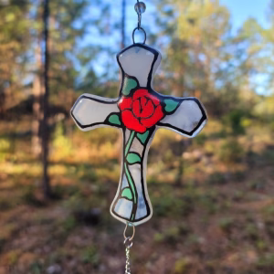 Red rose cross suncatcher with translucent white glass panels, green leaf detailing, and a hanging crystal accent, handcrafted with cremation ash.