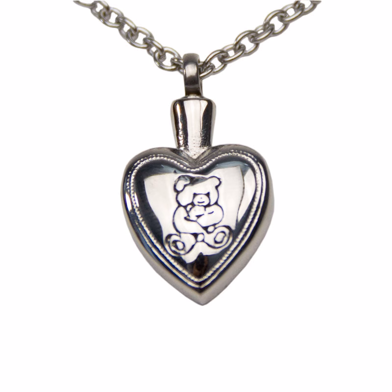 Close-up view of a silver heart-shaped cremation pendant engraved with a teddy bear design on the front, shown hanging from a silver chain.