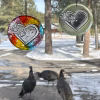 Two loving paw print heart glass suncatchers with encased cremation ash hanging in window, one multicolor and one clear, with snowy yard and wild turkeys outside