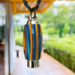 Hearthwood urn pendant with aqua fire laminate wood stripes and stainless steel core hanging from a black braided necklace outdoors with greenery and a wooden walkway in the background