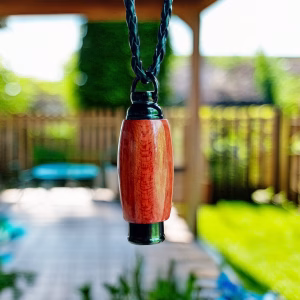Hearthwood urn pendant in bloodwood with black stainless steel core hanging from a braided cord outdoors