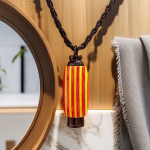 Hearthwood urn pendant with yellow and red striped wood hanging from a braided leather cord against a wood and marble background