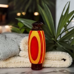 Hearthwood urn pendant with yellow and red layered wood grain surrounding a black stainless steel core standing upright on folded towels with green plants in the background