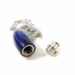 Hearthwood urn cremation pendant shown open with royal blue and charcoal laminate wood exterior, stainless steel threaded core opening, and detached screw lid beside pendant on white background