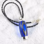 Hearthwood urn pendant with royal blue and charcoal laminate wood grain resting on a white fur background with black braided cord and silver chain extender, flat lay view