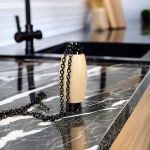 Hearthwood urn pendant in holly wood with black stainless steel core standing on dark marble countertop with black chain beside modern kitchen sink