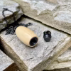 Hearthwood urn cremation pendant crafted from holly wood shown opened with removable black stainless steel threaded core beside the pendant on stacked stone