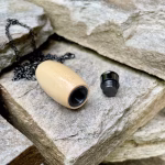 Hearthwood urn cremation pendant crafted from holly wood shown opened with removable black stainless steel threaded core beside the pendant on stacked stone