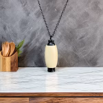 Hearthwood urn pendant in holly wood with black stainless steel core hanging on black chain above white marble countertop with wooden utensil holder in background