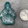 Top view of glass paw print cremation pendant in blended green and teal glass with encased cremation ash shown next to a quarter for size reference