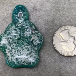 Top view of glass paw print cremation pendant in blended green and teal glass with encased cremation ash shown next to a quarter for size reference