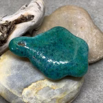 Back view of glass paw print cremation pendant in blended teal and green glass with encased cremation ash on stone background