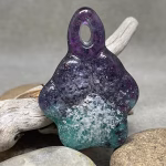 Glass paw print cremation pendant in blended purple and teal glass with encased cremation ash on stone background