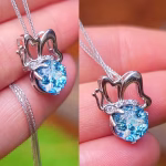 Close-up of a dichroic butterfly cremation pendant held between fingers, featuring a shimmering blue memorial stone infused with cremation ash set in a polished silver butterfly frame with delicate wing detailing, hanging from a fine silver chain