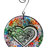 Loving paw print heart glass suncatcher with multicolor splatter design and encased cremation ash, hanging in window on metal hook