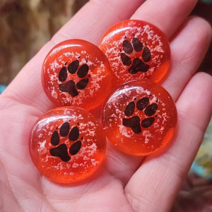Hand holding four red paw print cremation stones made of fused glass with embedded ash speckles