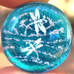 A turquoise-colored memorial glass stone with white cremation ash features 2 dainty white dragonflies.