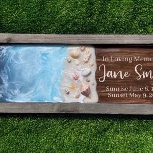 Framed oceanside memorial artwork featuring swirling blue resin waves blending into a sandy shoreline with seashells, personalized with the name Jane Smith and sunrise and sunset dates.