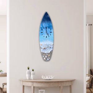 Oceanside surfboard-shaped memorial clock featuring a resin shoreline design with seashells and cremation ash, displayed hanging on a light-colored wall in a coastal-inspired room.
