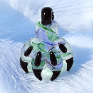 Glass paw cremation pendant with black paw pads and translucent green and lavender swirled glass resting on a soft white textured background