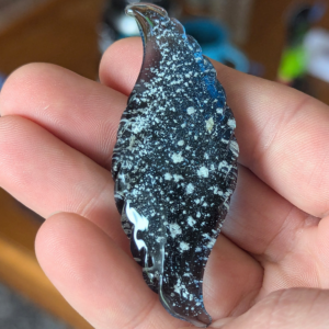 Wave shaped glass cremation touchstone with ashes featuring a flowing curved design and ribbed edges, handcrafted memorial stone held in hand for scale in natural light