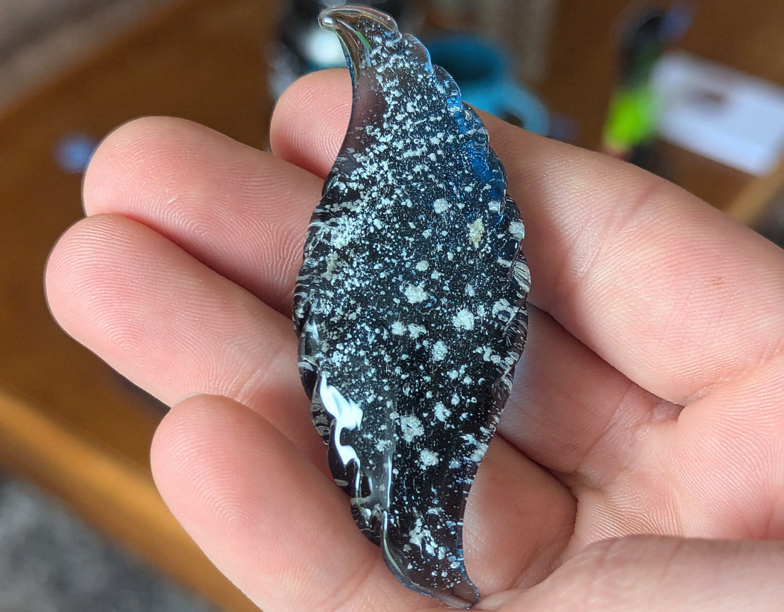 Wave shaped glass cremation touchstone with ashes featuring a flowing curved design and ribbed edges, handcrafted memorial stone held in hand for scale in natural light