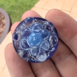 Blue sensory cremation stone with raised bubble texture and visible embedded cremation ash held between fingers outdoors