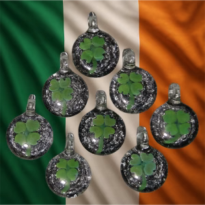Eight round glass four-leaf clover cremation pendants with silver bail loops arranged over an Irish flag background