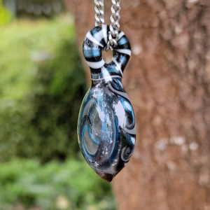 Clear oval glass pendant with blue and white spiral pattern hanging from a silver chain in front of a tree