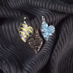 Three glass ribbon heart cremation pendants in yellow, blue, and soft black laid on dark textured fabric
