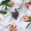 Black glass ribbon heart cremation pendant with soft rose tint and silver ribbon swirl detail on white marble background with pink flowers