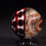 Handmade Shadow Marble with cremation ash featuring red and black patterned glass shown from side angle in studio lighting
