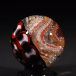 Handmade Shadow Marble with cremation ash featuring red and black patterned glass shown in studio lighting
