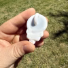 Back view of the white glass skull body and looped bail of the Stealie cremation pendant, fully showing the smooth white back surface while held between fingers outdoors over green grass