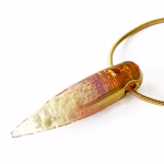Side view of a solid glass crystal cremation pendant with visible cremation ashes inside, featuring a clear-to-amber gradient created with pure gold fume and suspended from a gold snake chain.