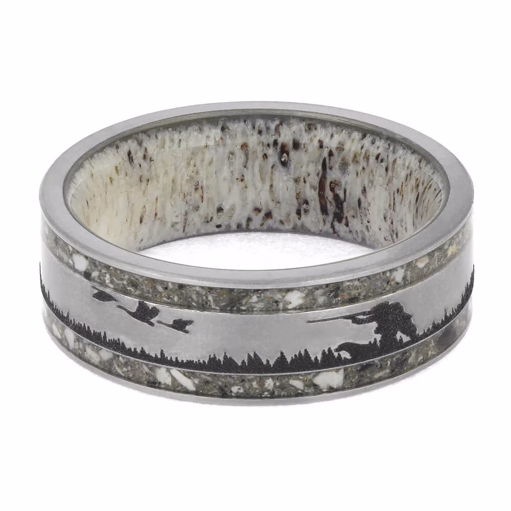 Inside view of hunting dog memorial ring with real antler interior, engraved hunter and bird silhouettes with tree line scene, and cremation ash inlays set into a brushed titanium band.