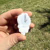Back view of the white glass skull body and looped bail of the Stealie cremation pendant, fully showing the smooth white back surface while held between fingers outdoors over green grass