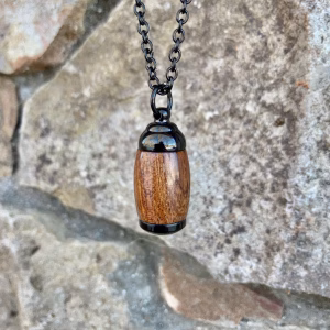 Straight-on view of an extra small Hearthwood urn pendant made from Hawaiian Koa wood with polished black metal end caps, suspended from a black chain for holding cremation ashes.