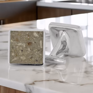 Angled front view of a pair of square memorial cuff links with light stone-textured inlay set in polished silver frames, with one cuff link facing forward and the other showing the hinged back, designed to hold cremation ashes.