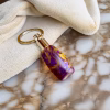 Angled overhead view of a royal honey aluminite memorial keychain featuring a marbled purple and gold resin body with a polished silver stainless steel core, resting on a marble surface with a folded cloth for holding cremation ashes.