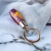 Angled side view of a royal honey aluminite memorial keychain featuring a marbled purple and gold resin body with a polished silver stainless steel core and attached metal key ring for holding cremation ashes.